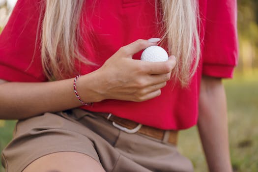 A close-up view of a woman in a red shirt holding a golf ball outdoors, capturing the essence of the sport.