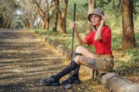 有纹身的女人坐在户外，手里拿着高尔夫球杆，戴着斗帽，穿着红色马球衫