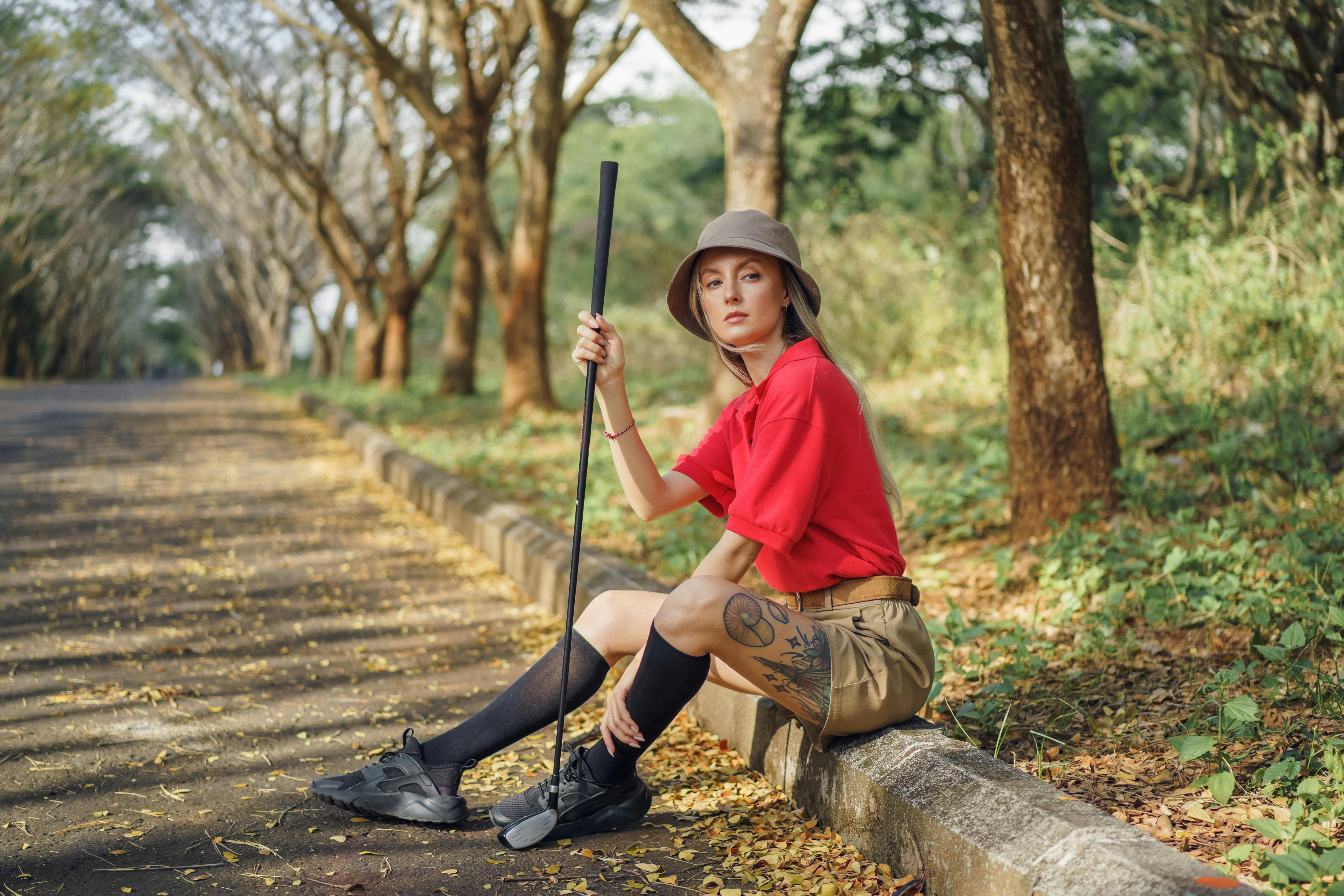 woman in red shirt and brown pants holding golf club