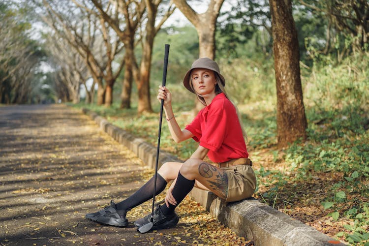 Woman In Red Shirt And Brown Pants Holding Golf Club