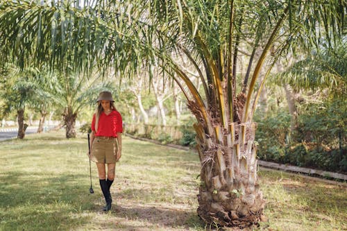 Young Woman with a Golf Club Walking under a Palm Tree 