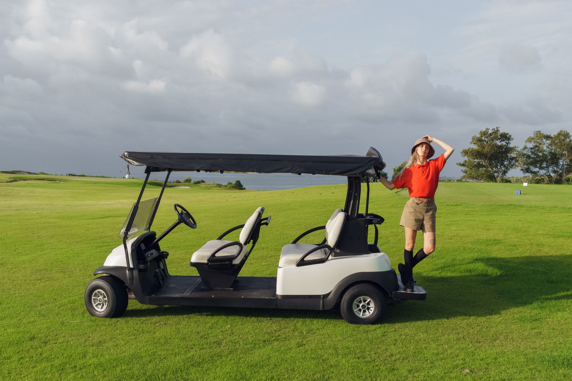 A woman in golf attire standing confidently beside a golf cart on a vibrant green golf course.