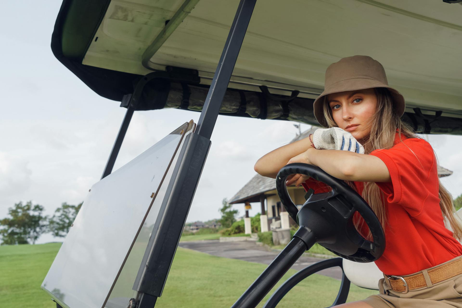 Chic woman in hat sitting in a golf cart on a lush green golf course.