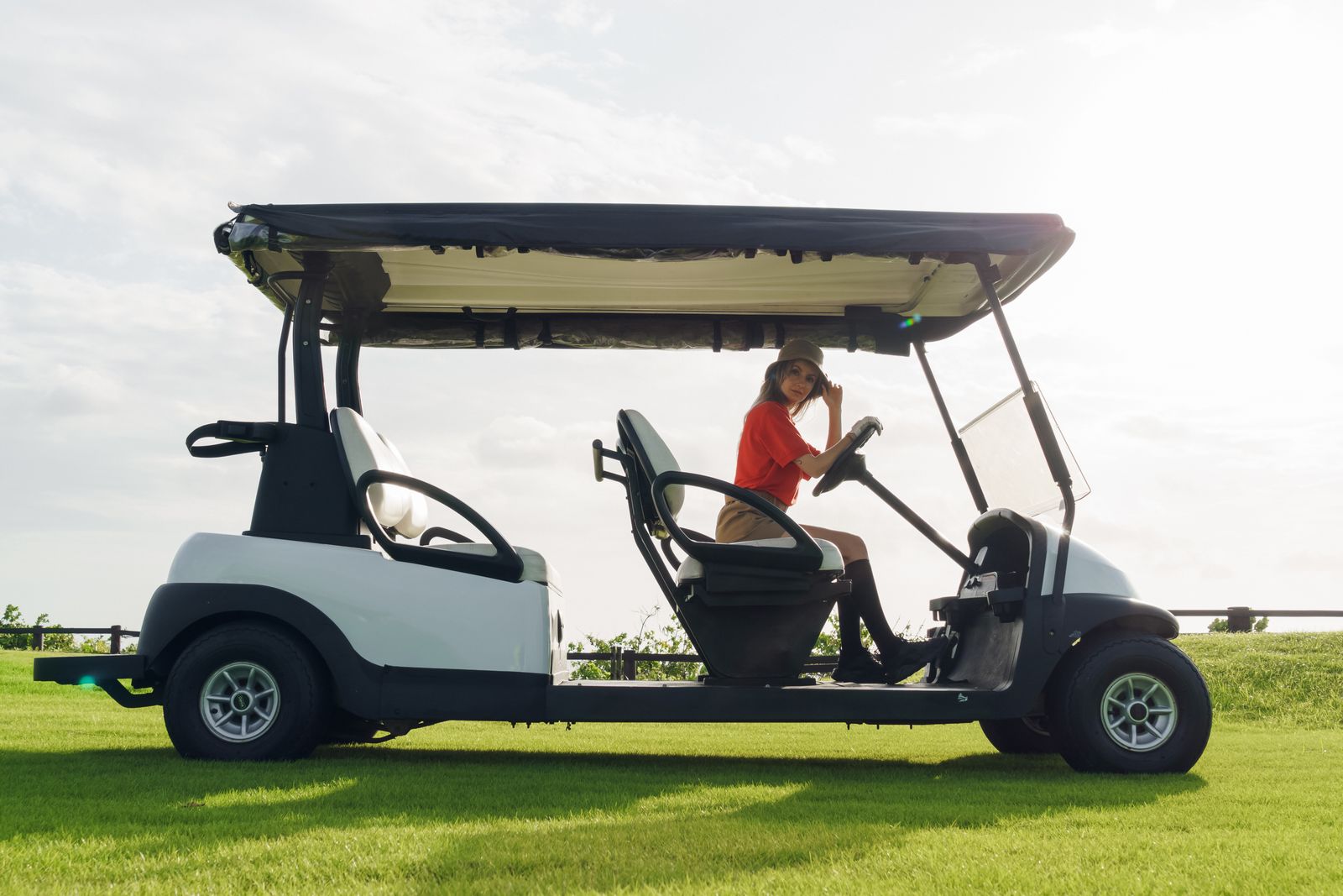 A woman seated on a golf cart at a sunny golf course, enjoying a leisure day outdoors.