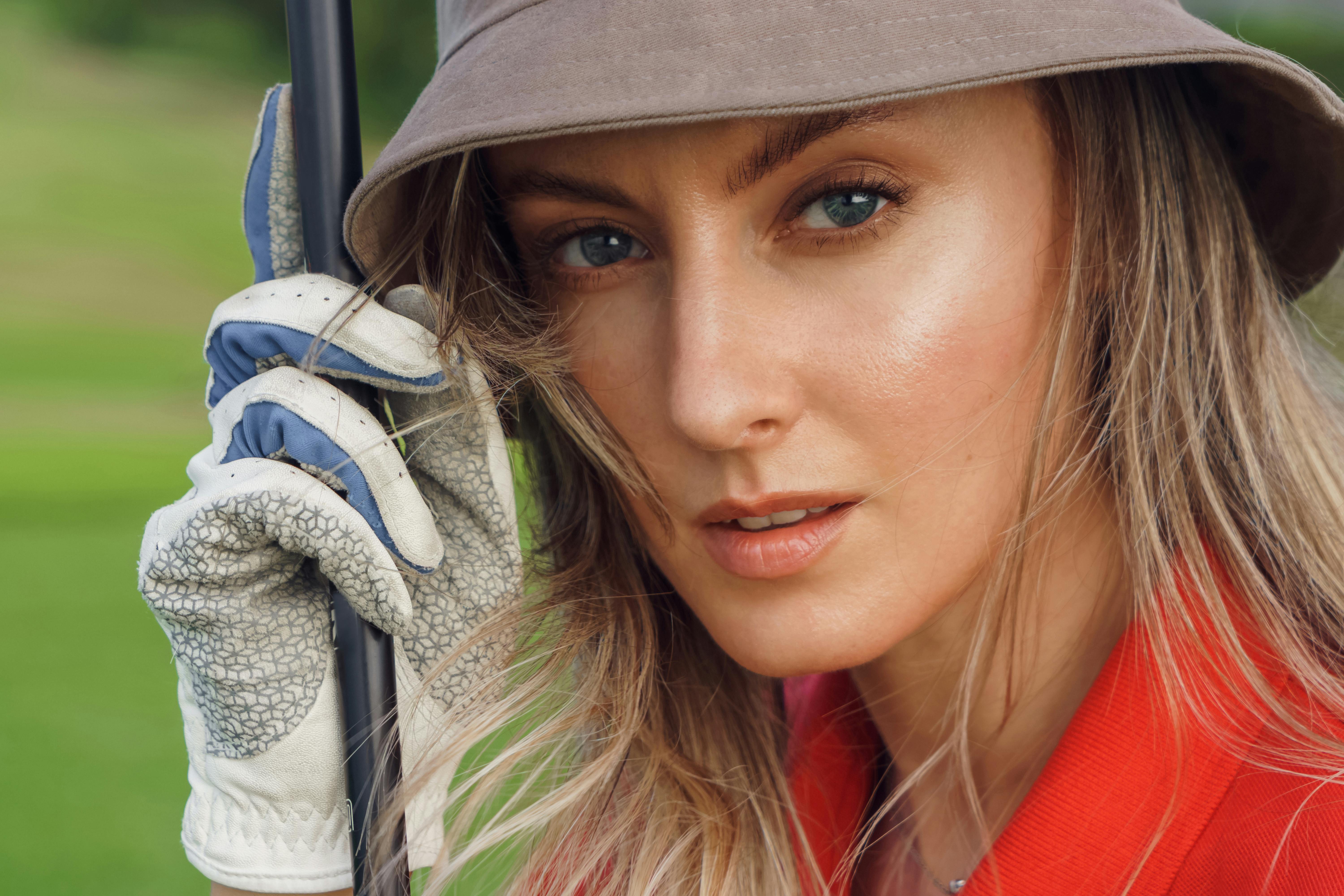 Close-up portrait of a woman with blonde hair and blue eyes, wearing a bucket hat and a golf glove.
