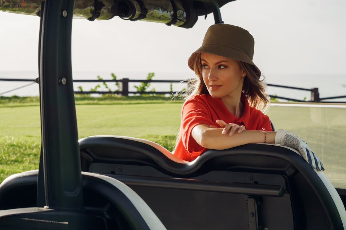 A woman in a hat overlooking her shoulder sitting in a golf cart