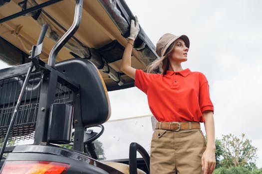 A woman wearing a red polo and bucket hat stands next to a golf cart. Captured outdoors in natural light.