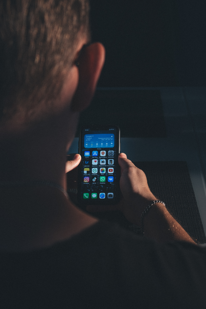 Close-up of a person holding a smartphone with apps visible on screen in a dimly lit environment