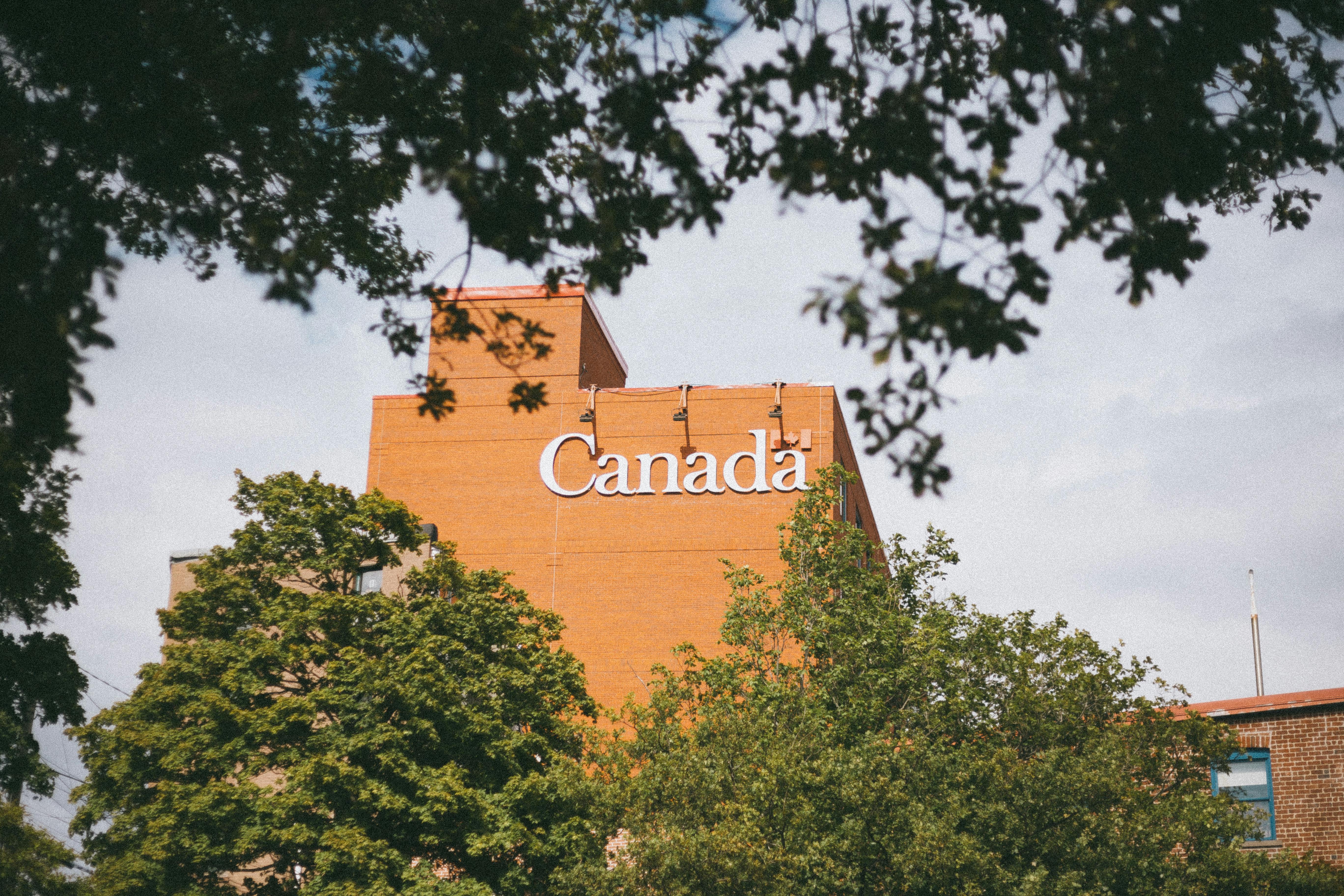 A brown building with Canada signage surrounded by greenery and tree branches.
