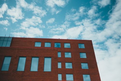 Free Low angle view of a modern brick building with glass windows and a blue sky backdrop. Stock Photo