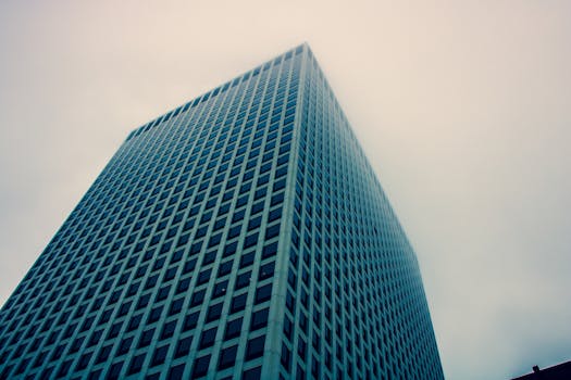 低角度视角下的现代摩天大楼，玻璃立面映衬着阴沉的天空