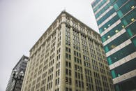 低角度拍摄城市环境中玻璃窗的当代摩天大楼，天空多云呈灰色