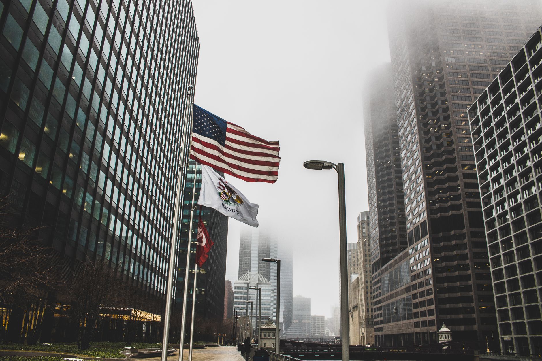 American flags waving in a foggy cityscape between modern skyscrapers.