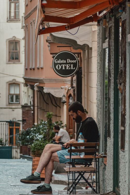Free Bearded man sits outside a cafe in old Istanbul, absorbed in his phone. Stock Photo