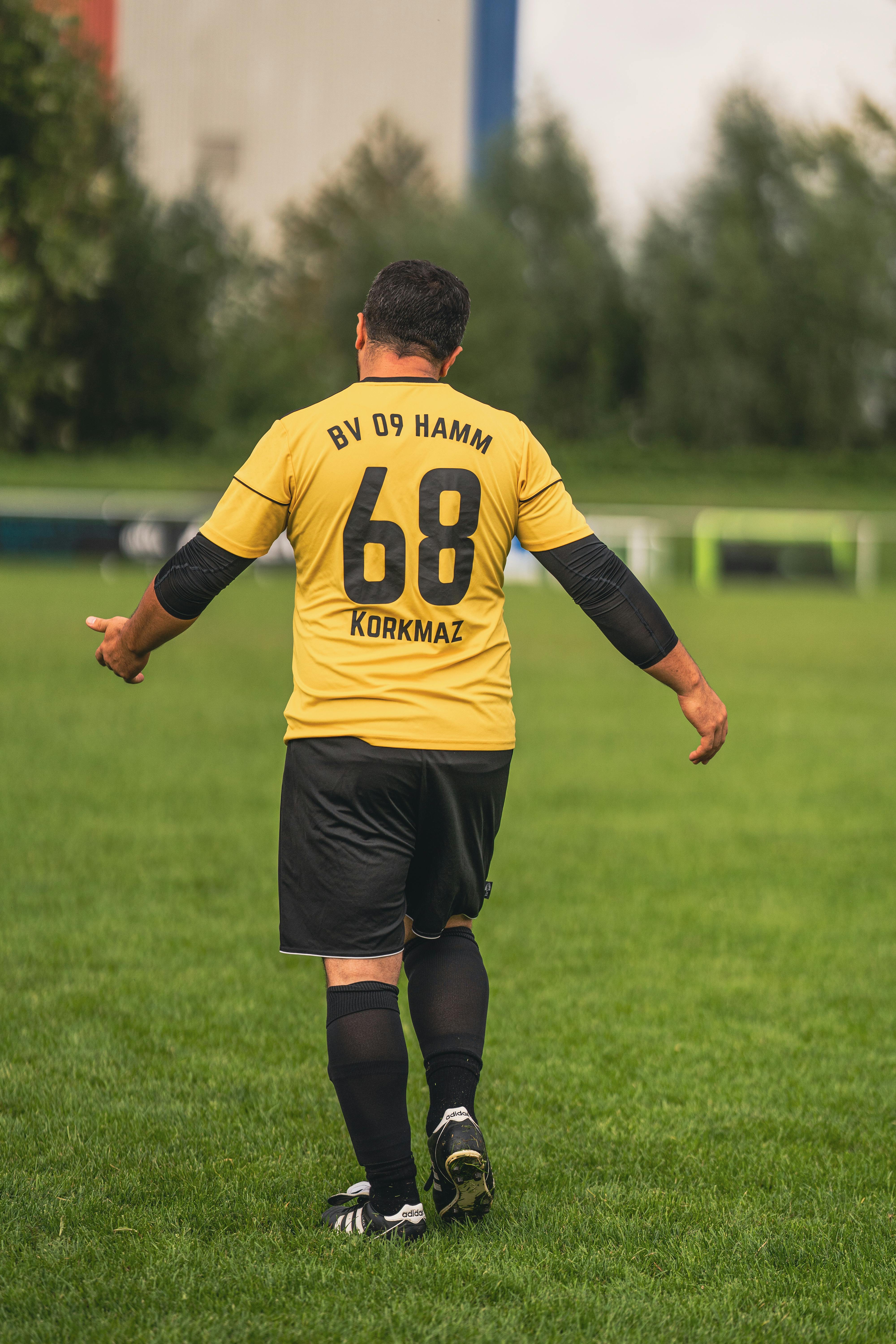 A male soccer player in a yellow jersey with number 68 walking on a football field.