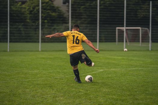 Back view of a football player in yellow jersey kicking a ball on a grass field.