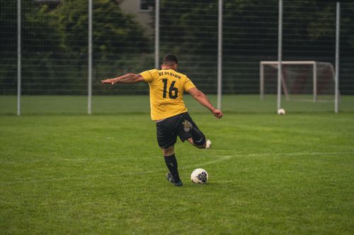 Free Back view of a football player in yellow jersey kicking a ball on a grass field. Stock Photo