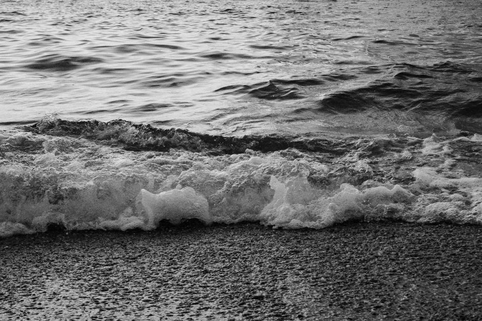 A monochrome photo of waves crashing onto a gravel beach, capturing the essence of nature.