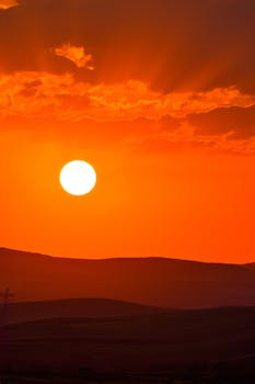 A breathtaking sunset with a vibrant orange sky over peaceful hills.