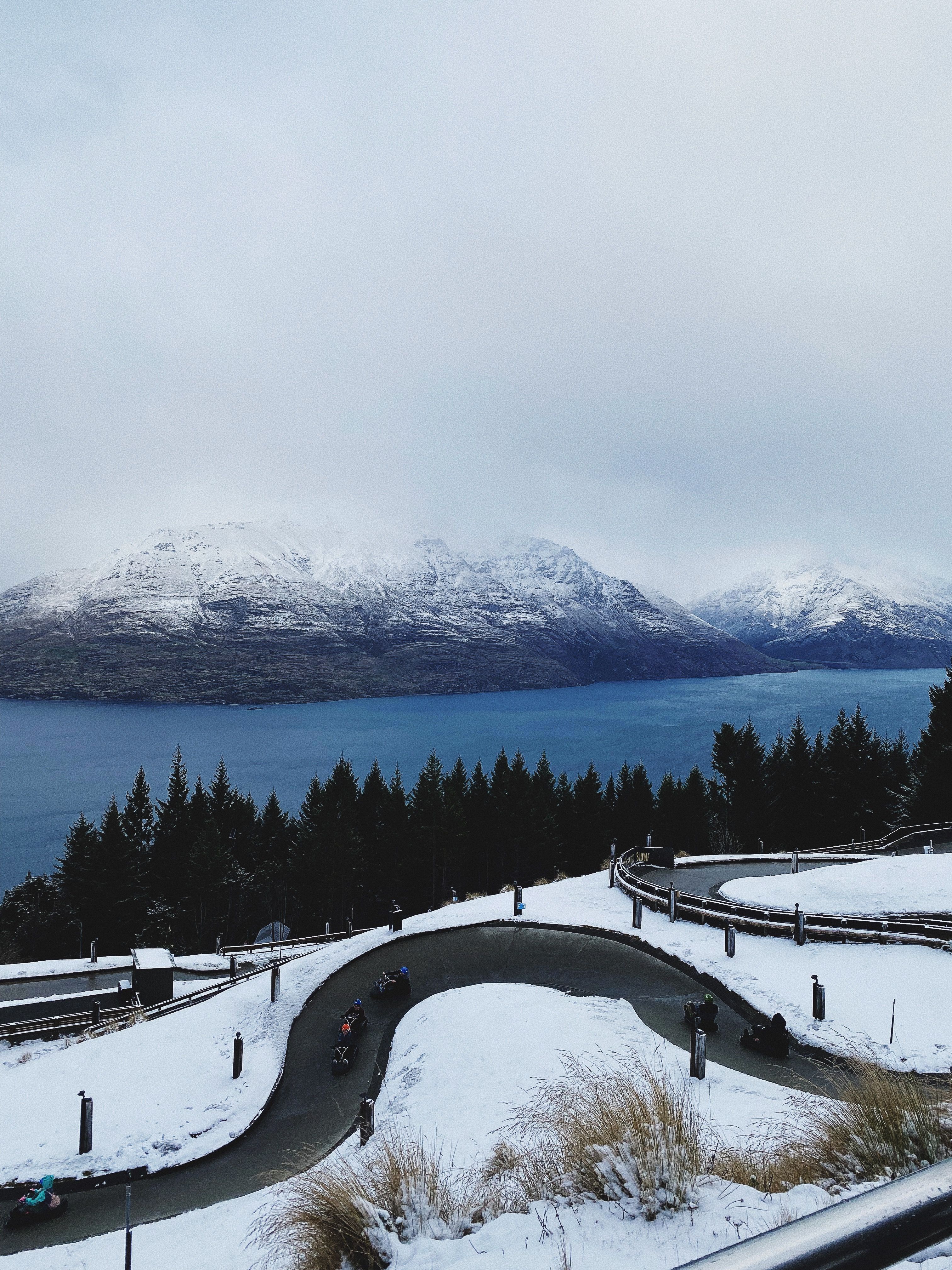 Scenic snowy view of winding road with mountains and lake in background.