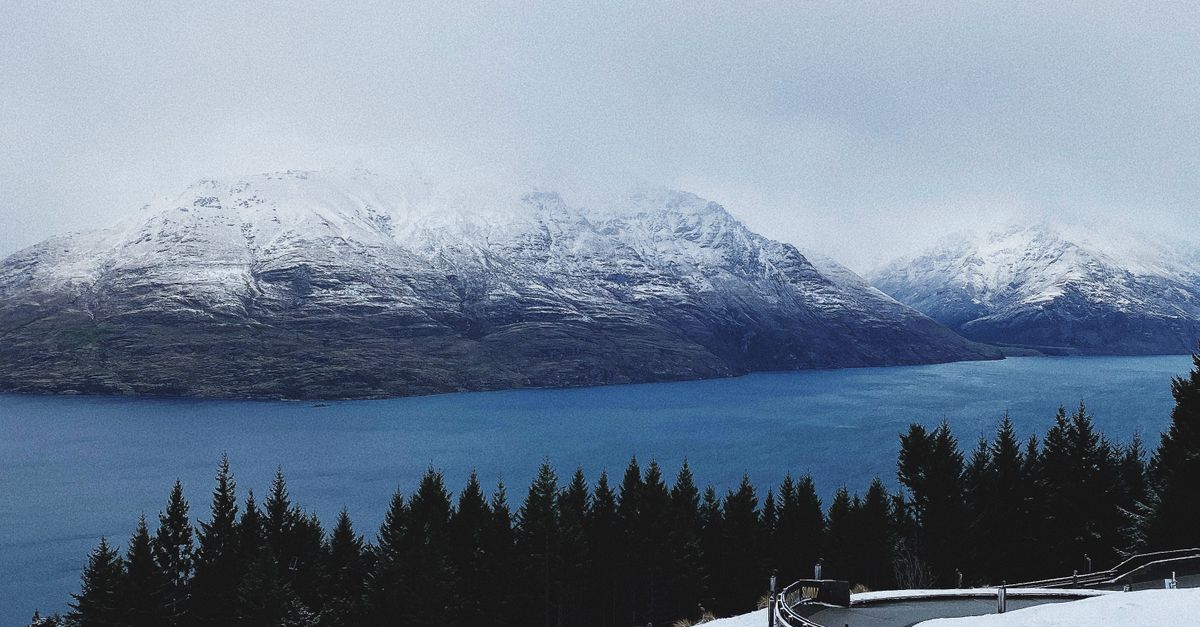 Scenic snowy view of winding road with mountains and lake in background.
