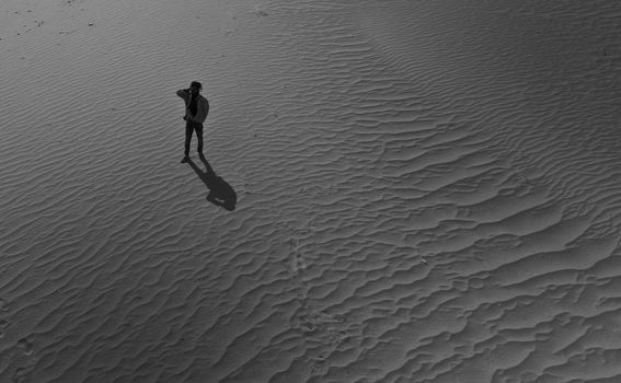 Black and white aerial view of a person standing alone in Hunder desert sand.
