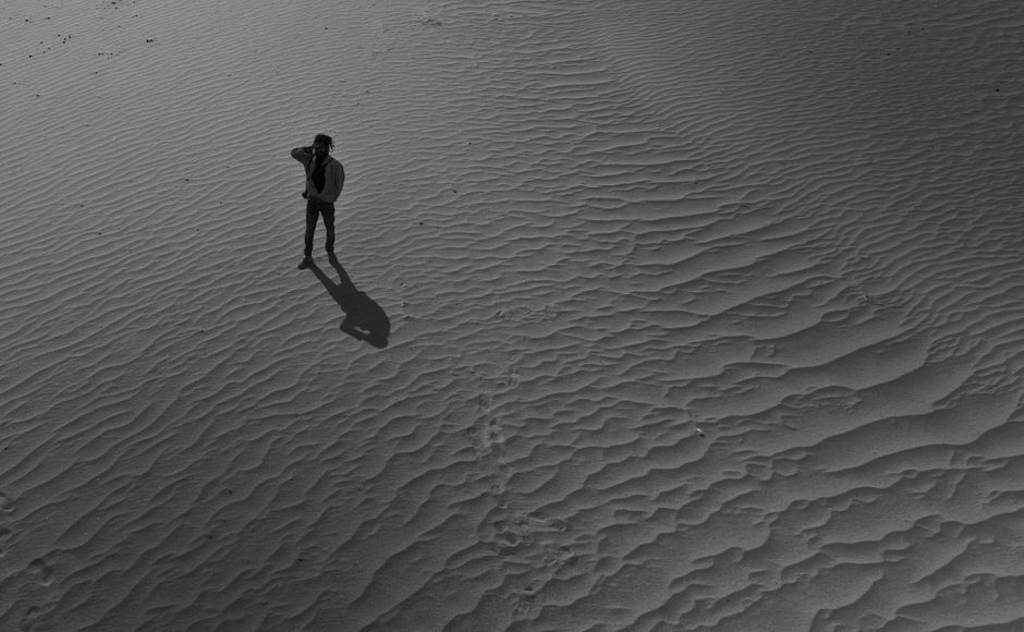 Black and white aerial view of a person standing alone in Hunder desert sand.