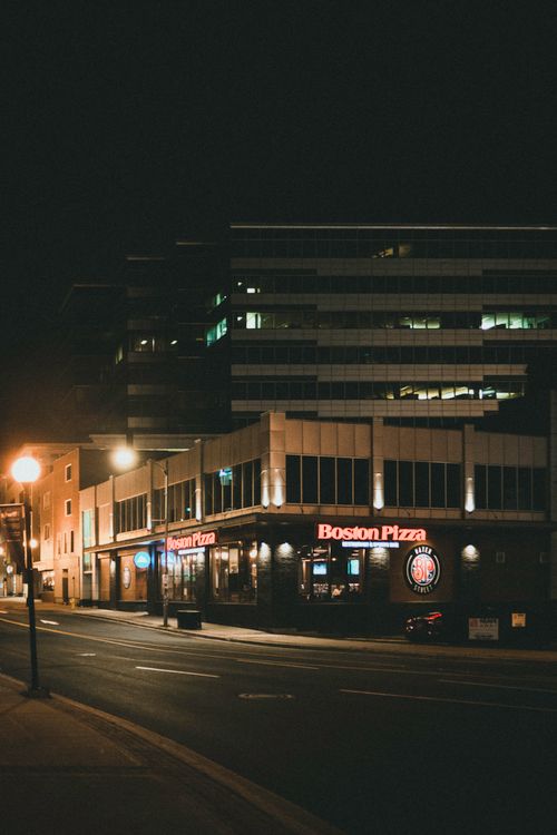 Free Urban street scene at night featuring a Boston Pizza restaurant exterior illuminated by street lamps. Stock Photo