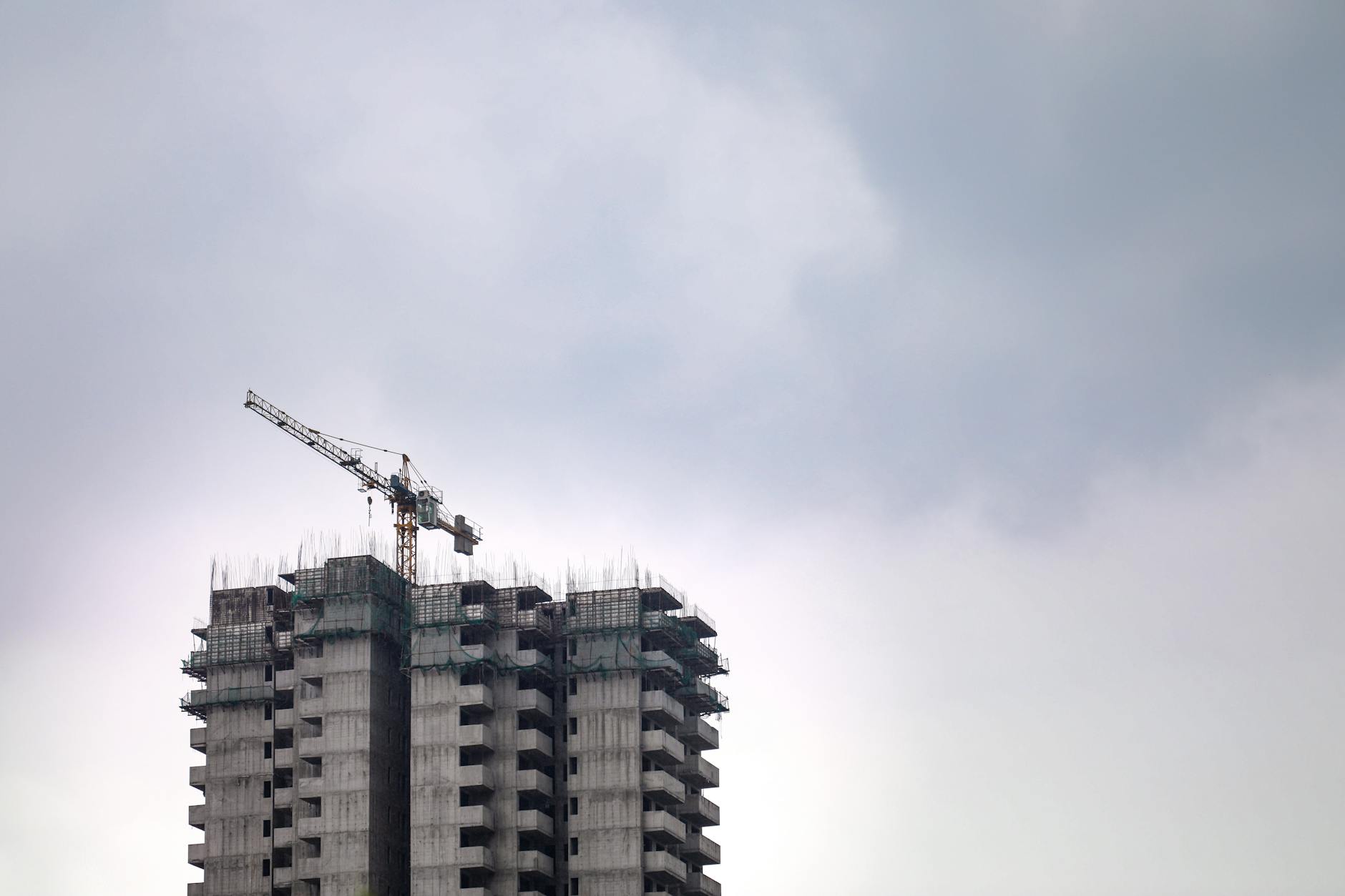 High-rise building construction site with crane against a cloudy sky, showcasing urban development.
