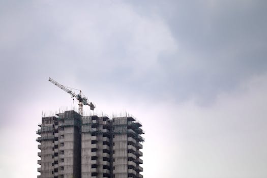 High-rise building construction site with crane against a cloudy sky, showcasing urban development.