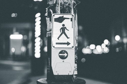 Free Grayscale image of a pedestrian crossing button on a city street at night with blurred lights in the background. Stock Photo