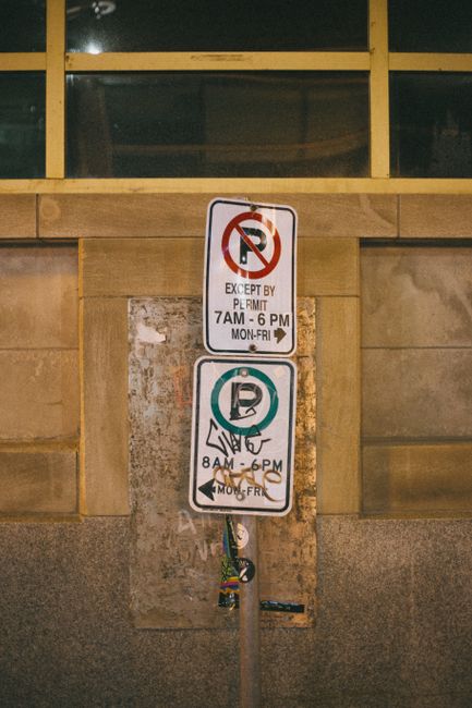Photo by Erik Mclean Nighttime urban shot of traffic signs with graffiti against a concrete wall.