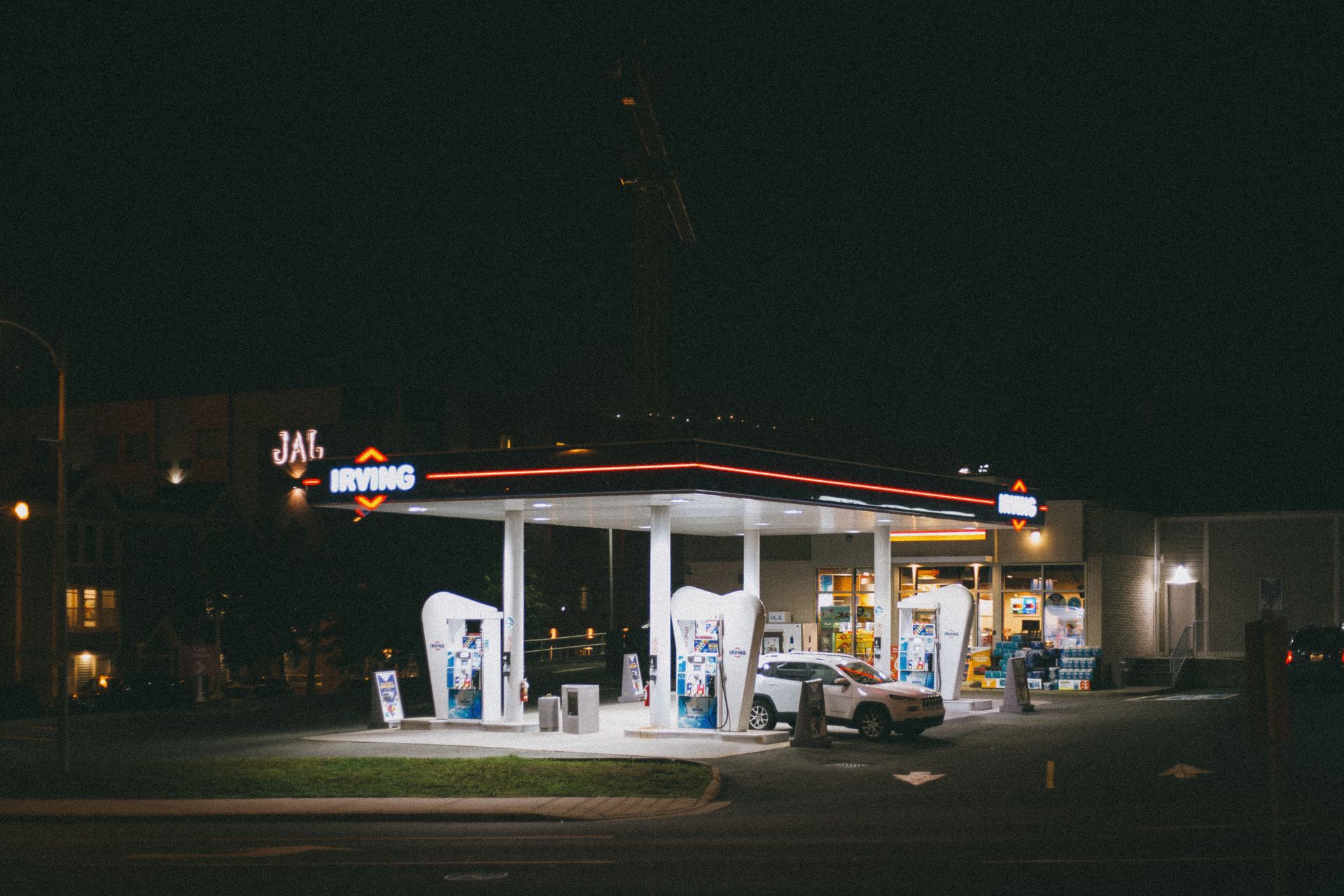 A brightly lit gas station with a car, captured under a dark night sky.