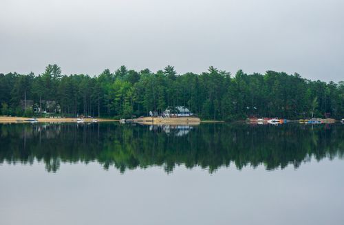 Free A tranquil lake reflecting lush green forests under a calm sky. Stock Photo