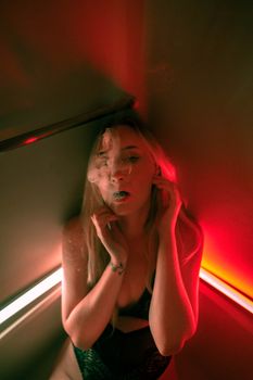 Moody portrait of a woman in lingerie enveloped in smoke and colored lights.