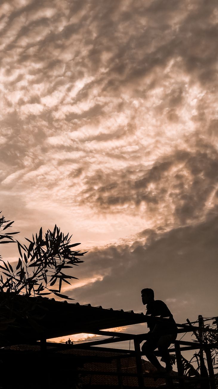 A dramatic silhouette of a person climbing a rooftop against a textured sunset sky.. dramatic, silhouette, person