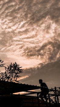 A dramatic silhouette of a person climbing a rooftop against a textured sunset sky.. dramatic, silhouette, person