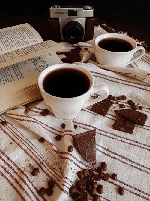 Free Warm still life of two ceramic cups of coffee, chocolate, coffee beans, book, and a vintage camera on a striped cloth. Stock Photo