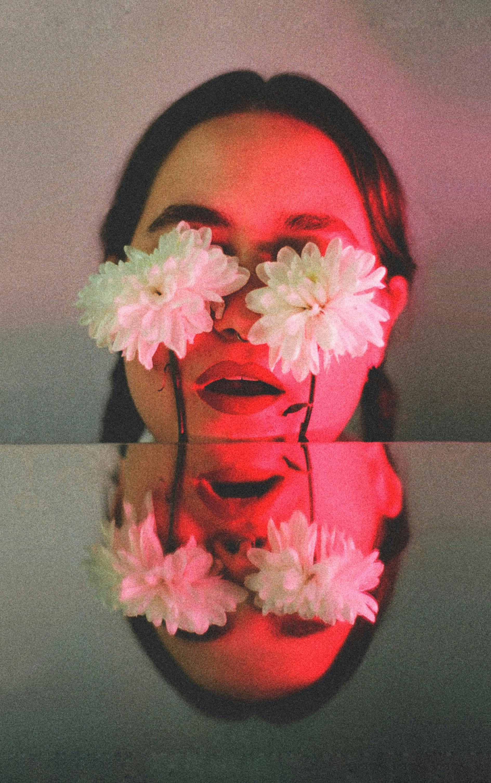 Artistic portrait of a woman with flowers covering her eyes, reflected in a mirror.