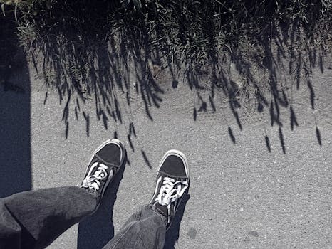 Top view of jeans and sneakers on concrete path with plant shadows in outdoor setting.