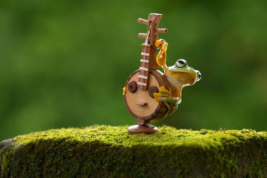 Adorable frog interacting with a miniature instrument on moss, set in nature.