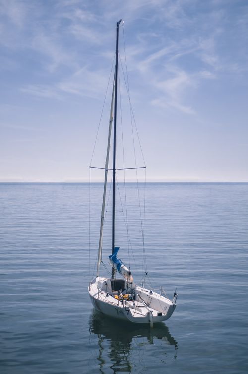 Free A serene sailboat gliding on a still ocean under a clear blue sky, offering a peaceful escape. Stock Photo