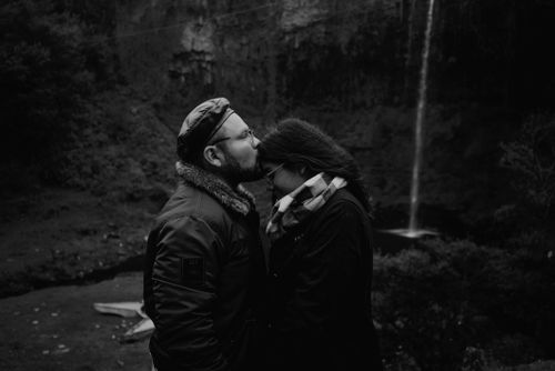 Free A couple shares a tender moment by a majestic waterfall in a grayscale setting. Stock Photo