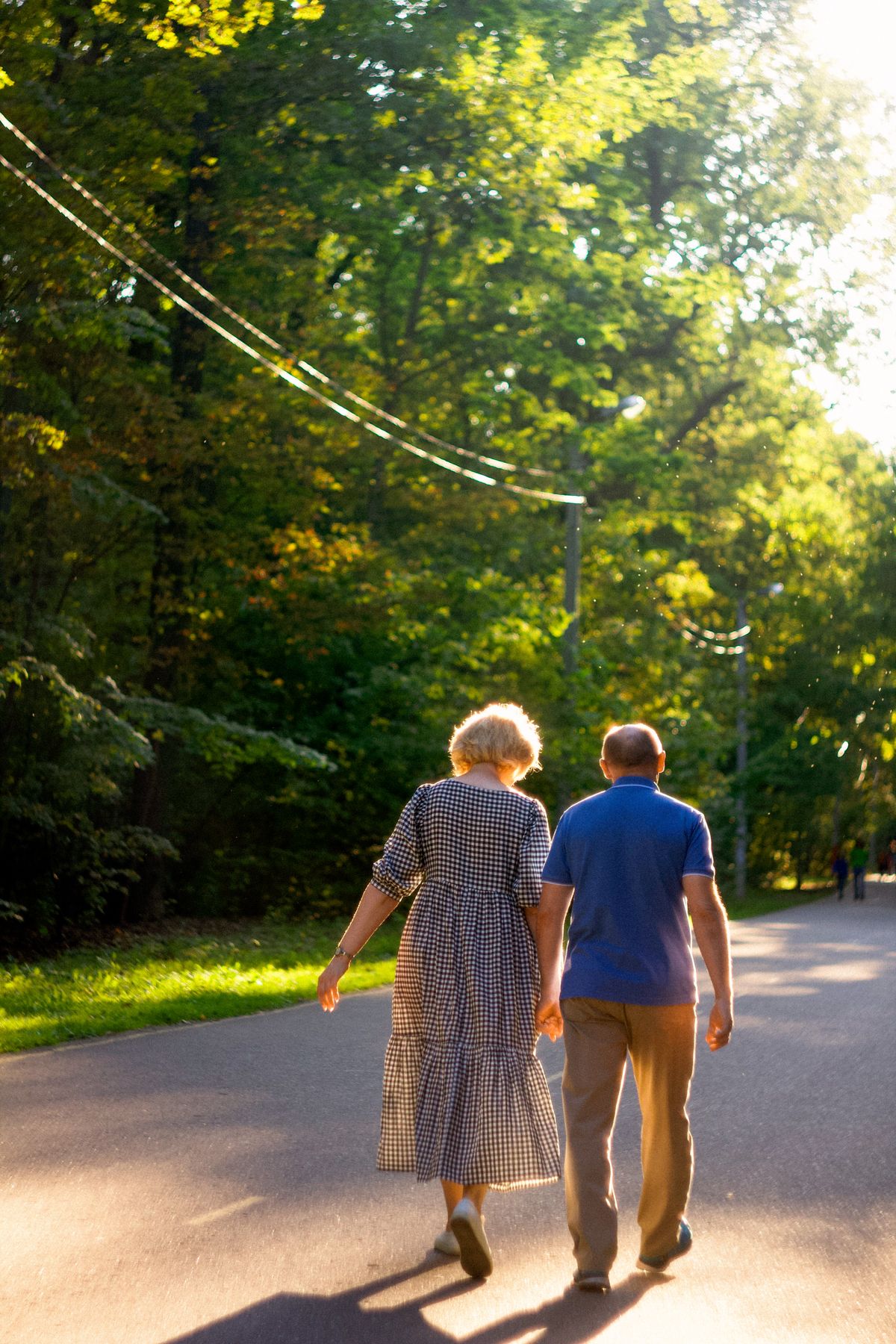 Active older couple walking hand in hand along a sunlit park path