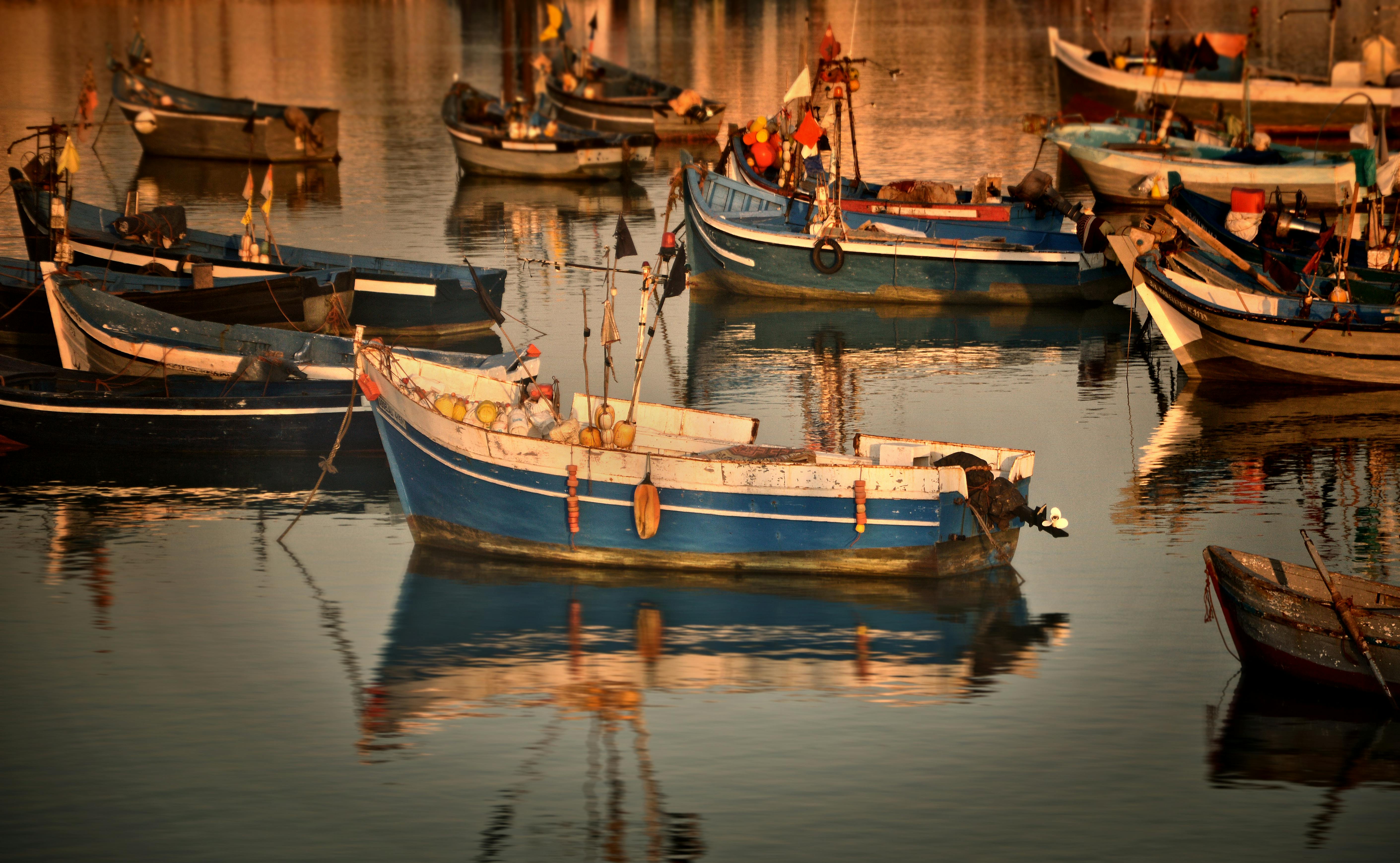 Free Colorful wooden fishing boats reflected in the calm waters of Asilah harbor, Morocco at sunset. Stock Photo