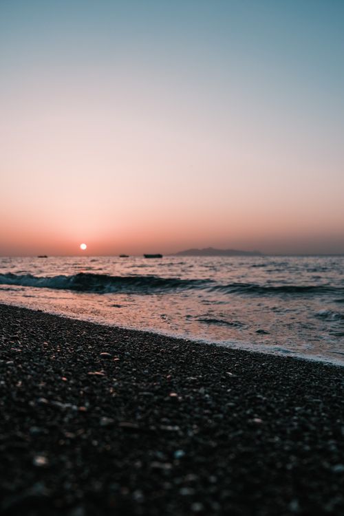 Free Peaceful beach scene captured during sunset with waves softly lapping the shore, offering a serene seascape view. Stock Photo