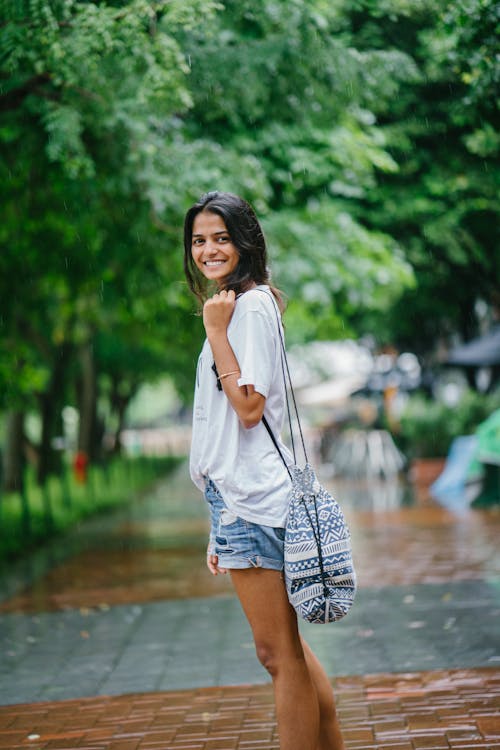 Shallow Focus Photography of Woman in White Shirt and Blue Denim Shorts on Street Near Green Trees