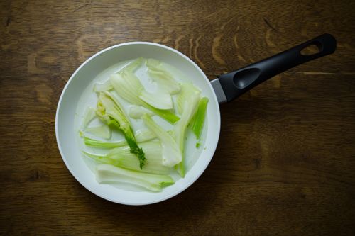 Free Sliced fennel bulbs in a frying pan, showcasing fresh ingredients on a wooden table. Stock Photo