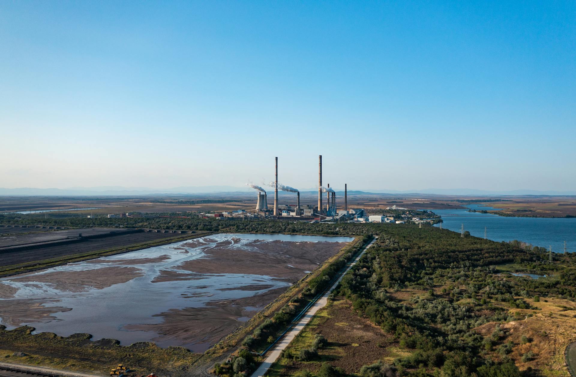Aerial view of an industrial plant emitting smoke, surrounded by nature.