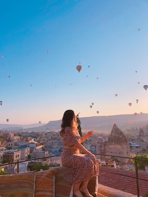 Free A woman sits, admiring hot air balloons over Cappadocia's sunrise. Captivating and serene. Stock Photo